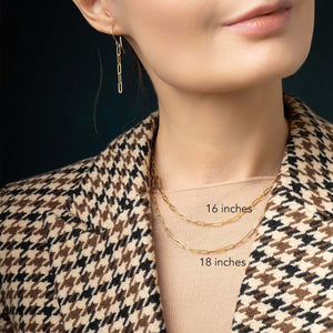 Close-up of a person wearing gold necklaces with measurements labeled, against a dark background.
