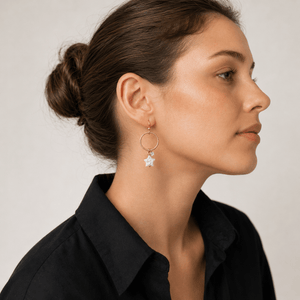 Woman wearing gold hoop earrings with a star detail on a neutral background