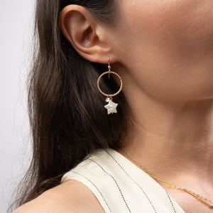 Close-up of a person wearing a gold earring with a star detail on a plain background