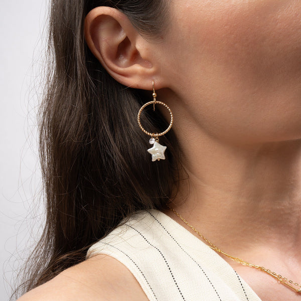 Close-up of a person wearing a gold earring with a star detail on a plain background