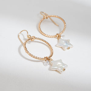 Gold hoop earrings with star-shaped pearl charms on a light gray background