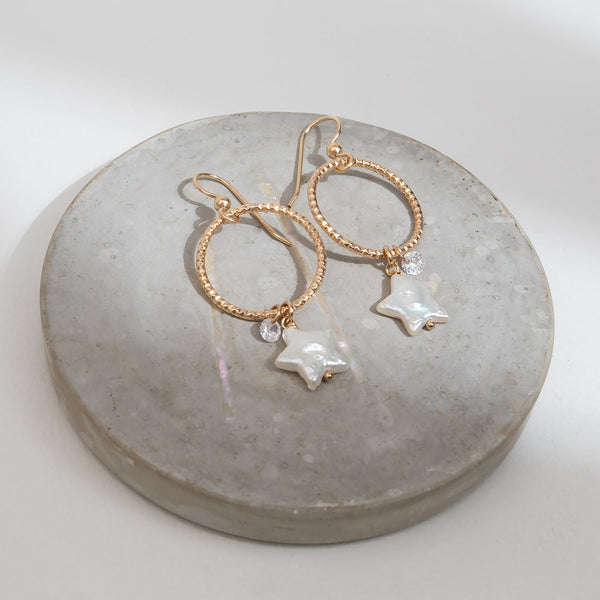 Gold hoop earrings with star-shaped charms on a concrete surface