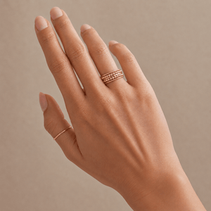 Hand wearing two gold rings on a beige background