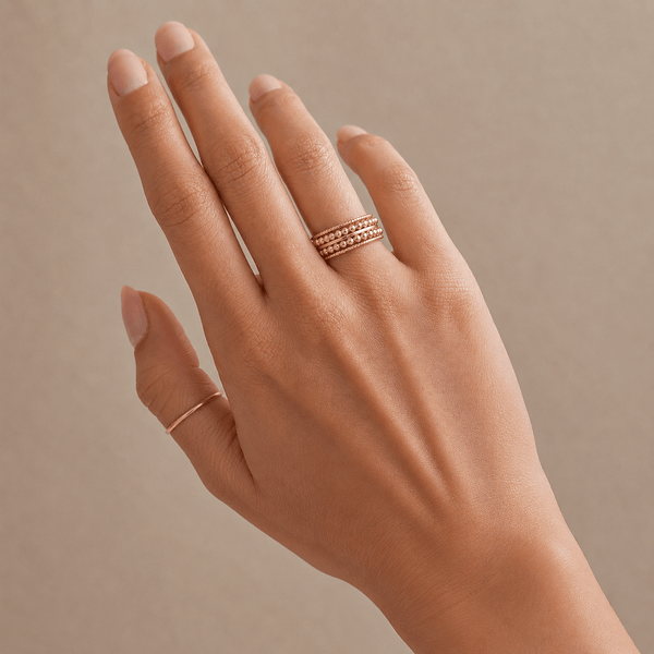 Hand wearing two gold rings on a beige background