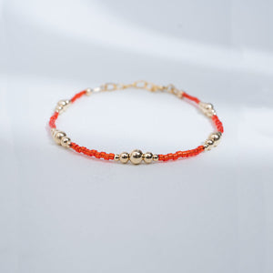 Bracelet with red and gold beads on a light gray background