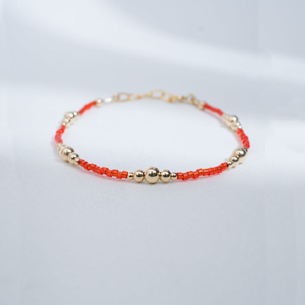 Bracelet with red and gold beads on a light gray background