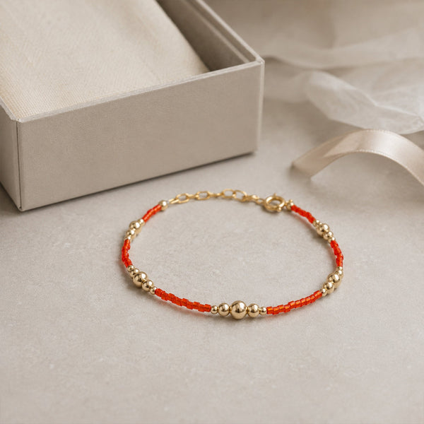 Bracelet with red and gold beads on a light gray surface