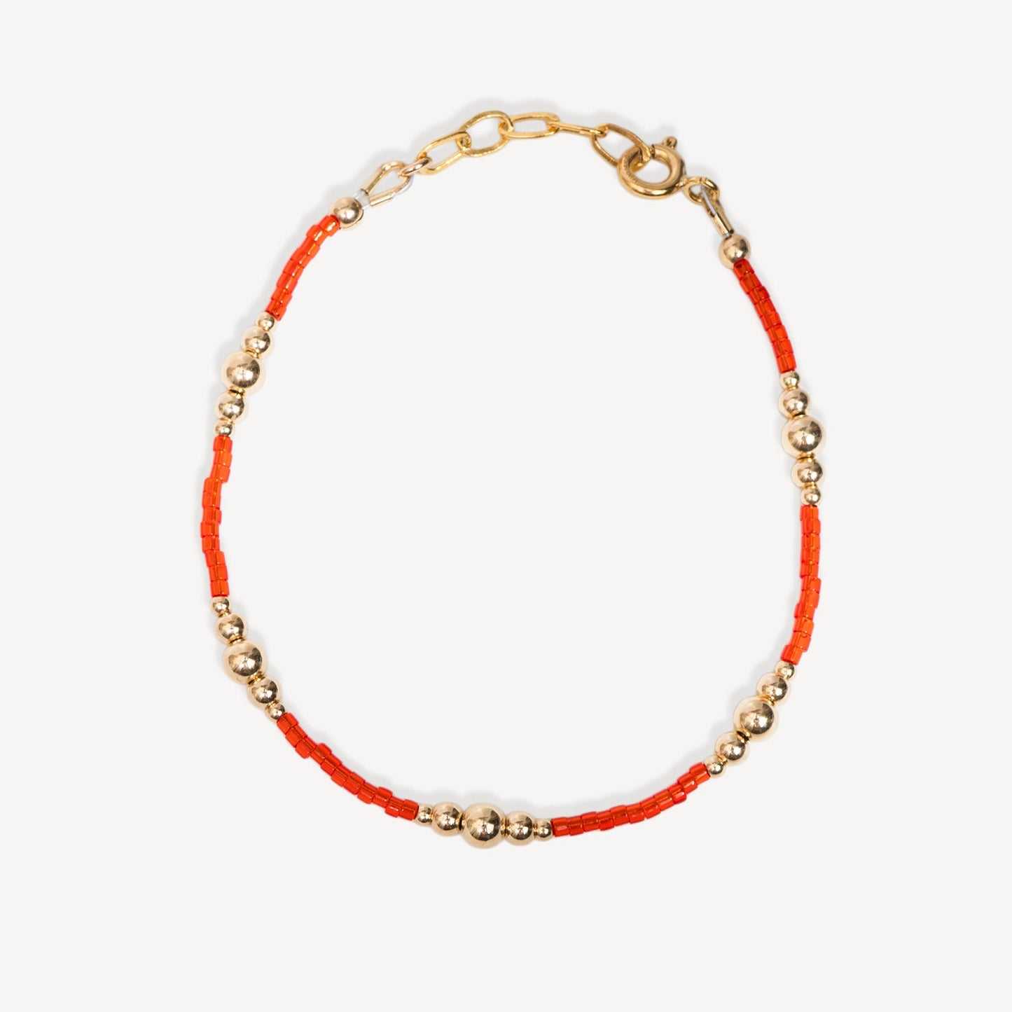 Bracelet with orange thread and gold beads on a white background