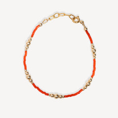 Bracelet with orange thread and gold beads on a white background