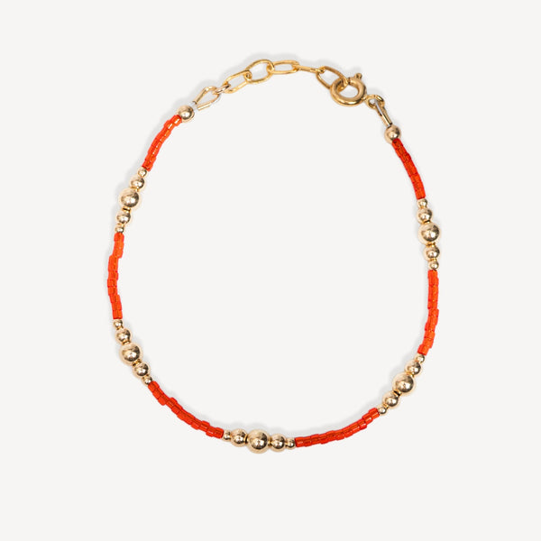 Bracelet with orange thread and gold beads on a white background