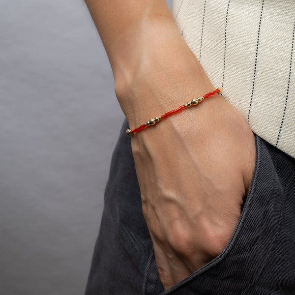 Close-up of a wrist wearing a red bracelet with gold beads against a neutral background