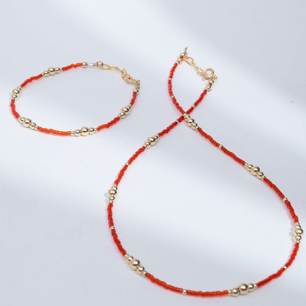 Necklace and bracelet set with red beads and gold accents on a white background