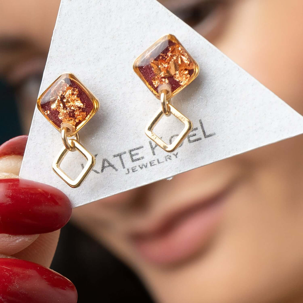 Gold earrings with square-shaped amber stones on a white background