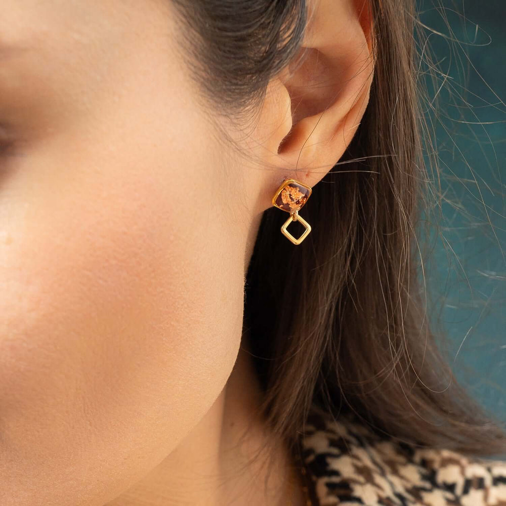 Gold earrings with square-shaped amber stones on a white background