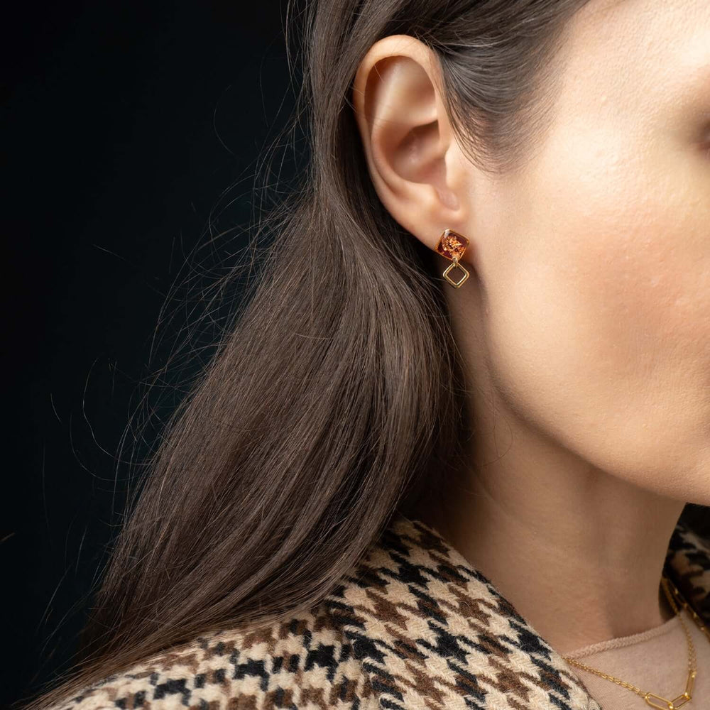 Gold earrings with square-shaped amber stones on a white background