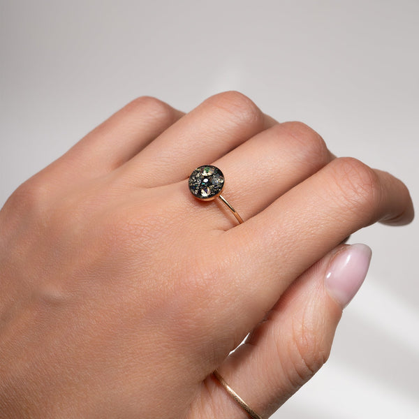 Hand wearing a ring with a dark gemstone on a neutral background