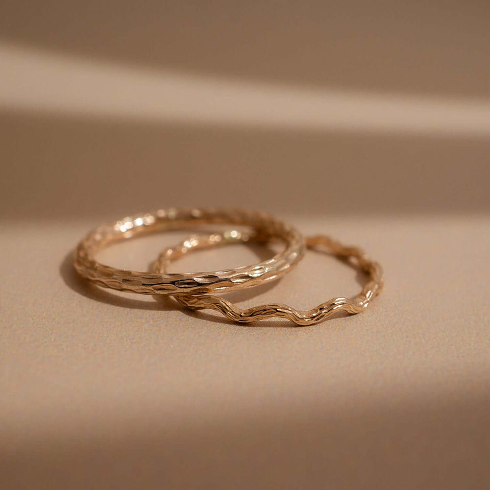 Two overlapping hammered metal rings in a warm gold tone, photographed on a clean off-white background.