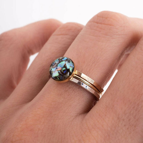 Rose gold ring with a colorful gemstone on a hand against a white background