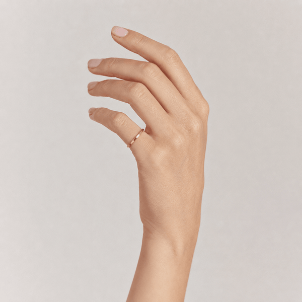 Hand wearing a gold ring on a plain background