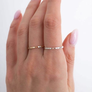 Hand wearing two thin gold rings on a white background