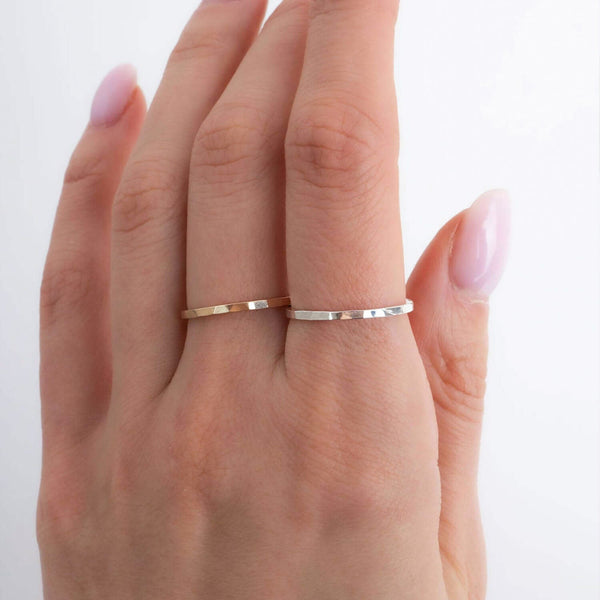 Hand wearing two thin gold rings on a white background