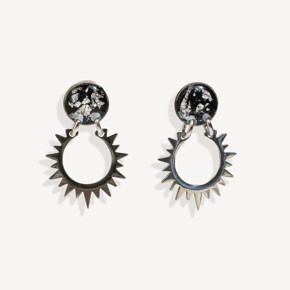 Pair of sun-shaped earrings with black and silver details on a white background