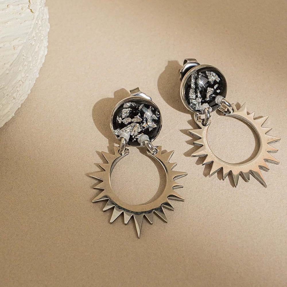 Pair of sun-shaped earrings with black and silver details on a white background