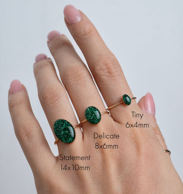 Hand wearing three green gemstone rings with size labels on a light gray background
