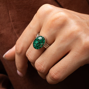 Close-up of a hand wearing an malachite ring on a brown background