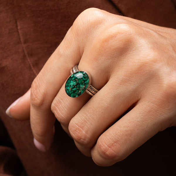 Close-up of a hand wearing an malachite ring on a brown background