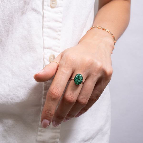 Hand wearing a green ring with a white shirt background