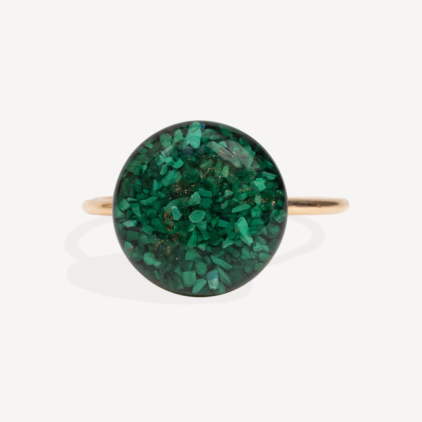 A gold band ring featuring a large, round cabochon stone filled with sparkling green glitter, set against a clean white background.