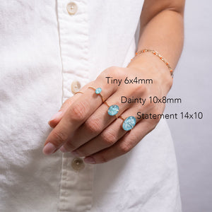 Hand wearing three different sizes of turquoise rings on a white shirt background