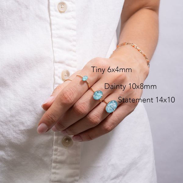 Hand wearing three different sizes of turquoise rings on a white shirt background
