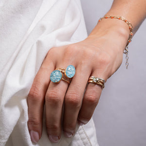 Hand wearing two gold rings with blue gemstones on a white background