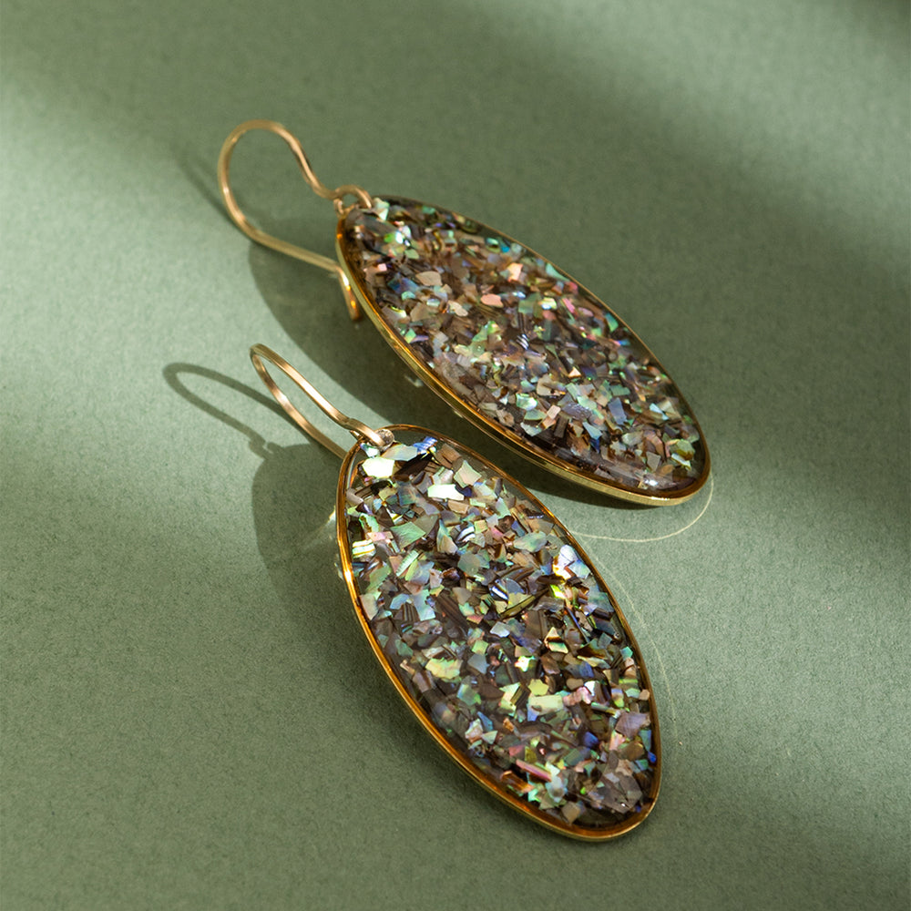 Oval-shaped earrings with a glittery, multicolored finish on a green background