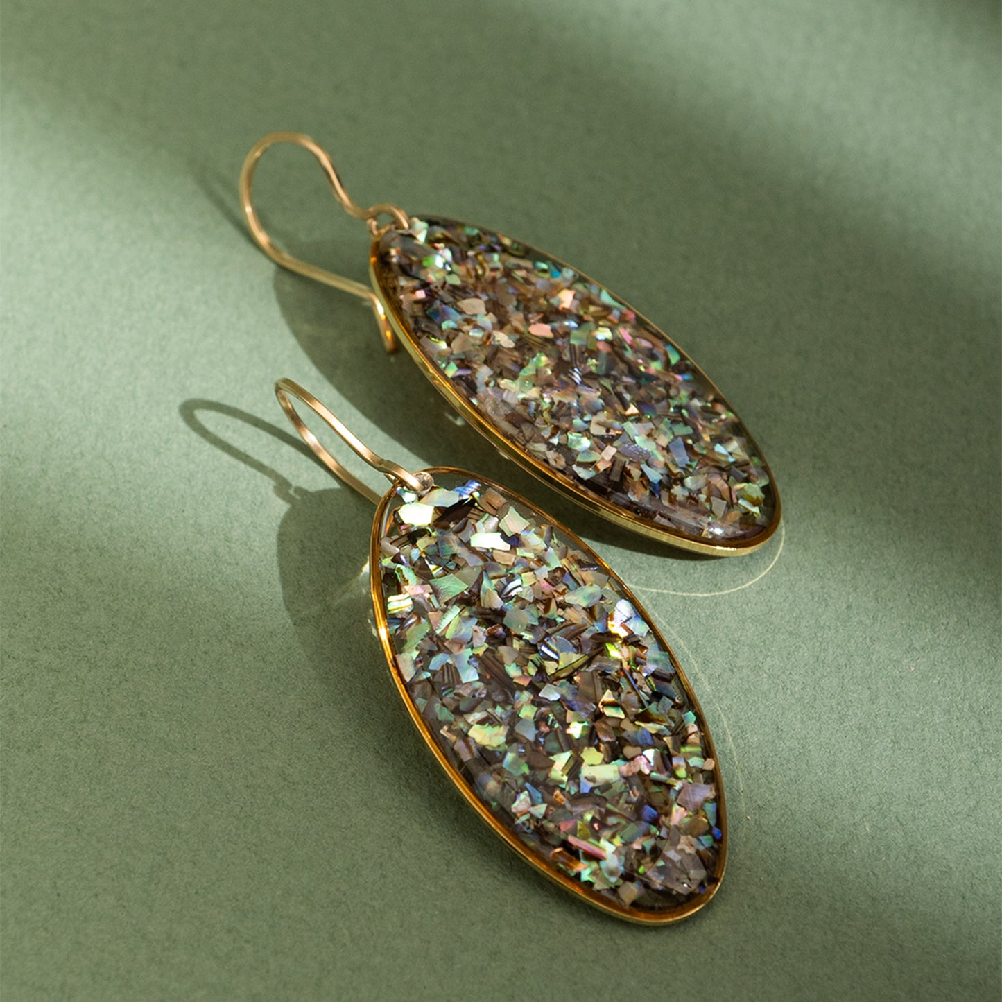 Oval-shaped earrings with a glittery, multicolored finish on a green background