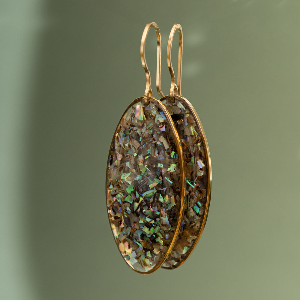 Gold earrings with iridescent stone on a green background