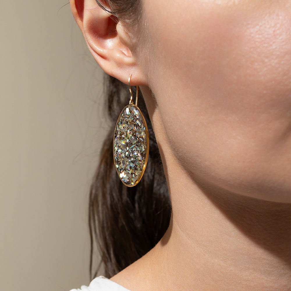 
                      
                        Close-up of a person wearing a gold and crystal earring against a neutral background
                      
                    