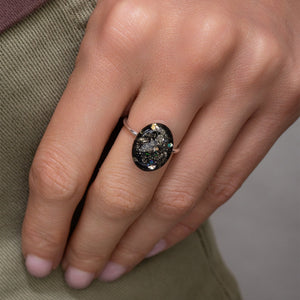 Close-up of a hand wearing a ring with a dark gemstone on a neutral background