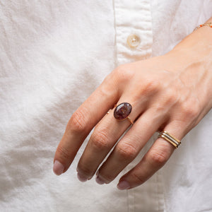 Hand wearing a ring with a brown gemstone on a white shirt background