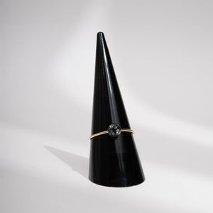 Gold ring with a green gemstone on a black cone against a gray background