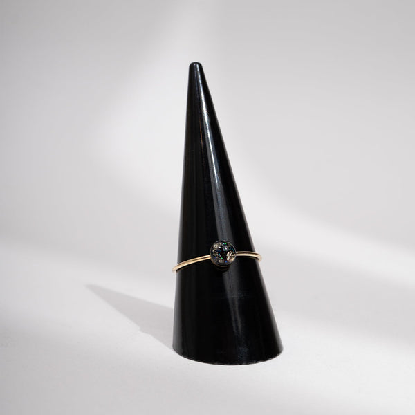 Gold ring with a green gemstone on a black cone against a gray background