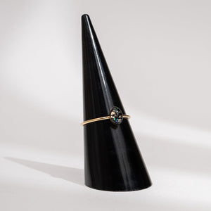 Gold ring with a gemstone on a black cone-shaped stand against a light gray background