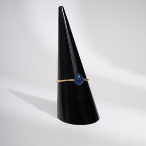Ring with a blue gemstone on a black cone stand against a white background