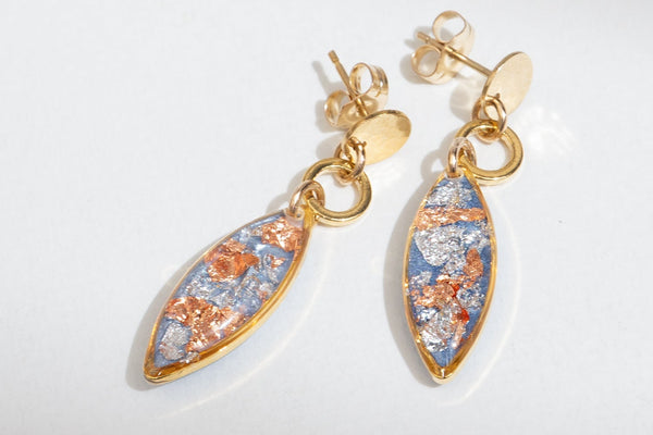 A pair of gold drop earrings with marquise-shaped charms featuring a textured, metallic blue, copper, and silver foil pattern, displayed on a clean white background.