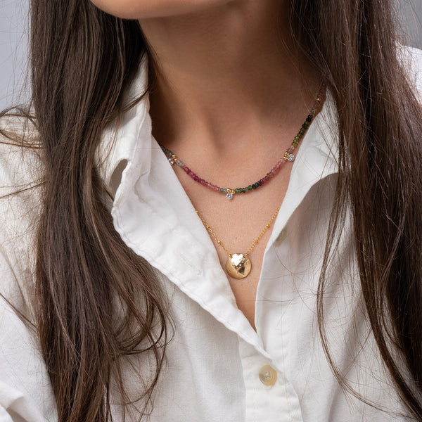 Close-up of a person wearing a white shirt and multiple necklaces with a neutral background