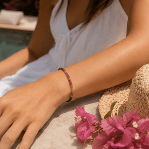 Person wearing a watermelon tourmaline bracelet with pink flowers and a straw hat in the background