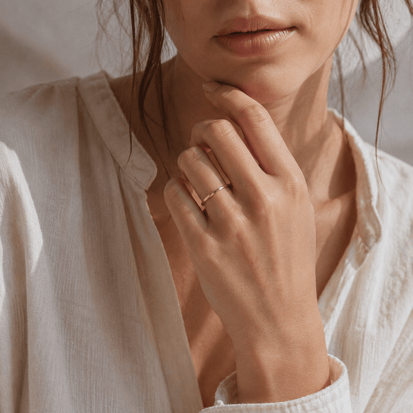 Close-up of a person wearing a gold stackable ring on a neutral background
